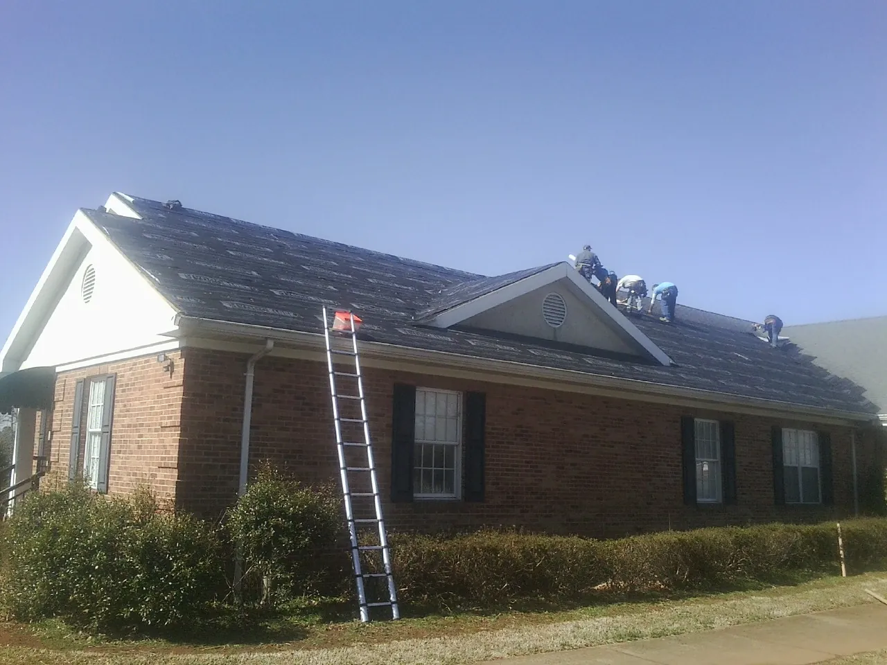 Crew tearing shingles off a brick ranch roof with a ladder set — Metal Roof Repair work by our crew in Parkersburg