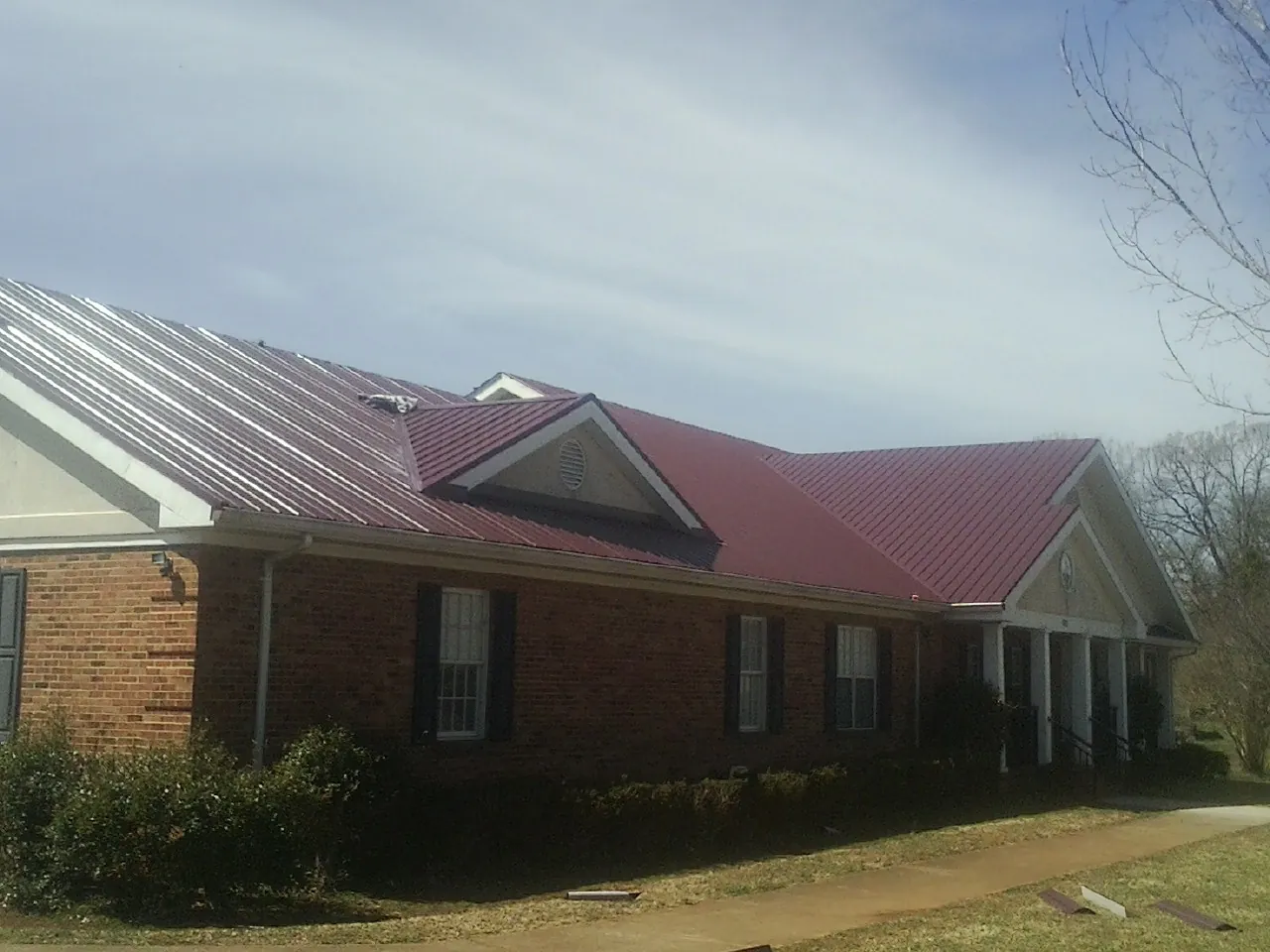 Red metal roof with gabled entries on a long brick building, from a Hail Damage Roof Repair job in Parkersburg