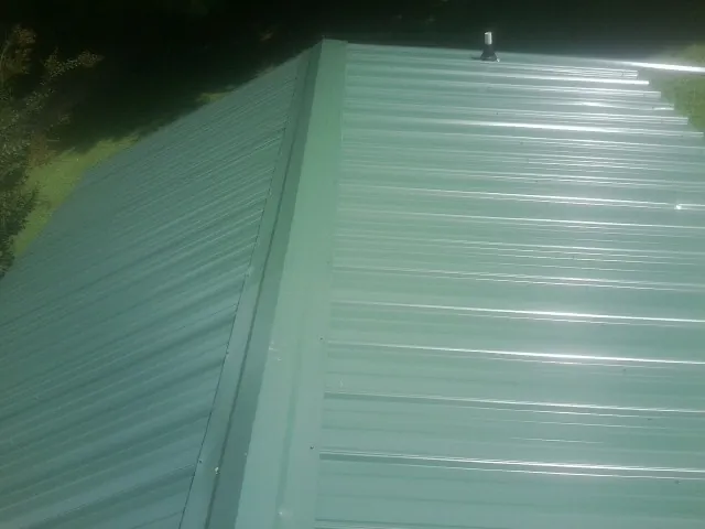 New green metal panels meeting at the ridge of a roof — Flat Roof Repair work by our crew in Parkersburg