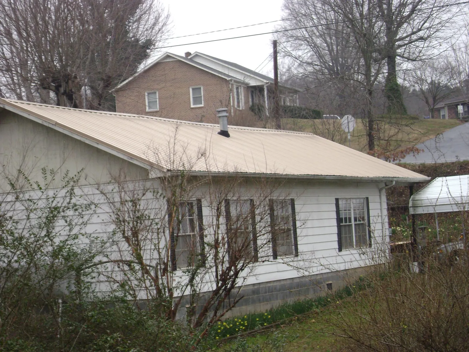 Tan metal roof on a white sided house set into a hillside — Commercial Roofing by Roofing Brothers in Parkersburg